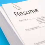 A pile of resumes with a paperclip sits on top of a cyan blue background.