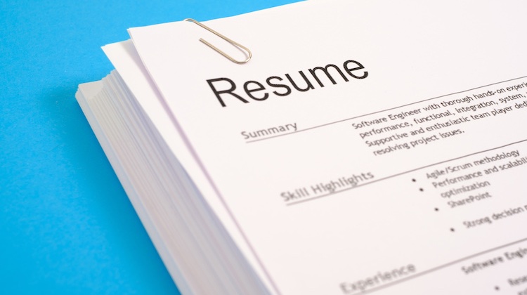A pile of resumes with a paperclip sits on top of a cyan blue background.