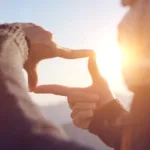 Person silhouetted in front of sunset forming a square with their fingers