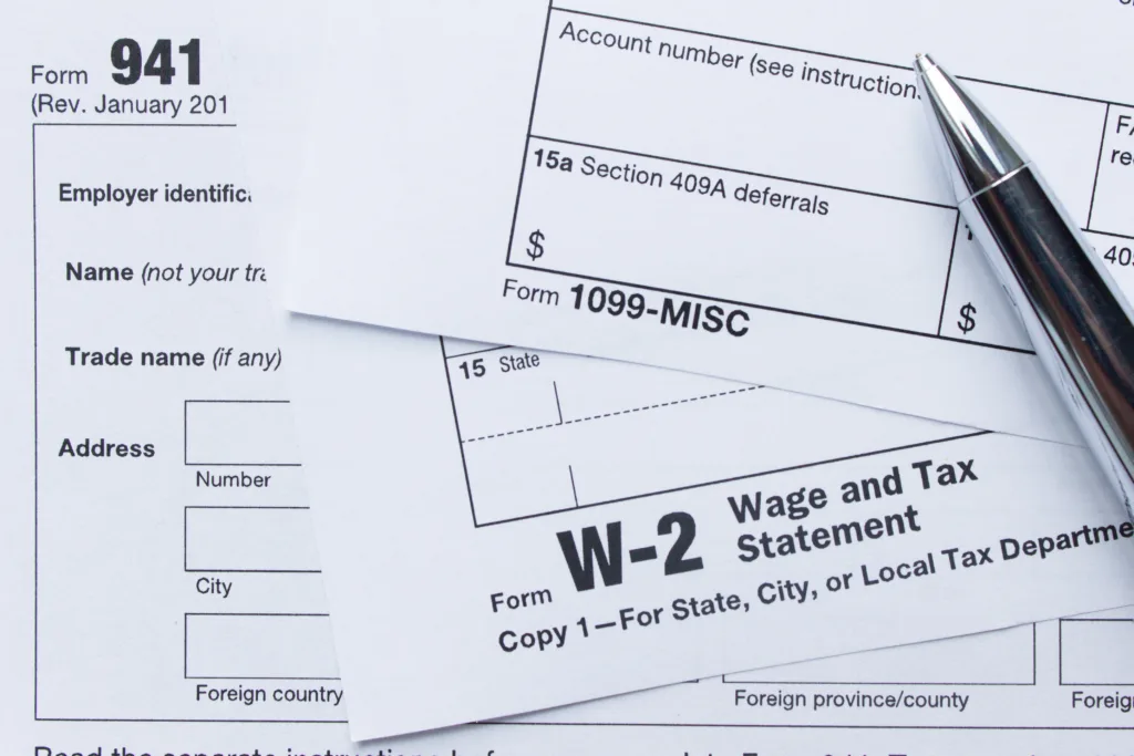 W-2 and 1099 tax forms with a pen resting on top; the #1 tax mistake freelancers make is not saving enough