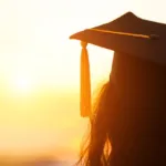 Silhouette of a woman wearing a graduation cap staring into a setting sun; portfolio schools aren't the only way to become a copywriter