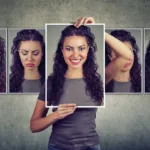 7 photos in a row against a concrete wall of a woman making different faces from frustrated to sad, but she stands behind the image in the middle holding it up of her face smiling.