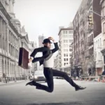 Man in suit holding a briefcase runs across a city street