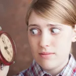 Blonde woman looks scared while gazing at an alarm clock