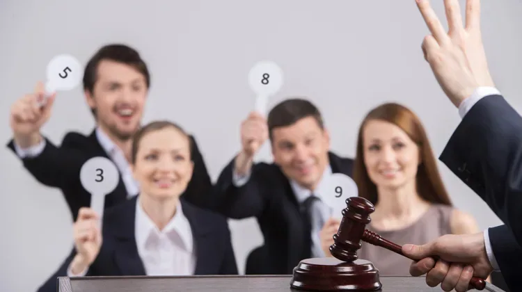 A group of four people all in blazers, two men and two women hold up paddles with numbers on them while a hand in the foreground holds up three fingers.