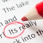 Red colored pencil hovers over word "Its" (which should be it's), which is circled in red on a typed sheet of paper.