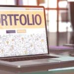 Laptop flipped open with the word "Portfolio" at the top in big block letters.