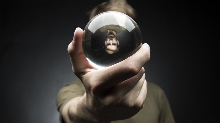 A young man holds a glass sphere in an outstretched hand, his reflection appears upside down.