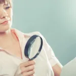 Woman in a short-sleeved pink colored shirt holds a magnifying glass to a document