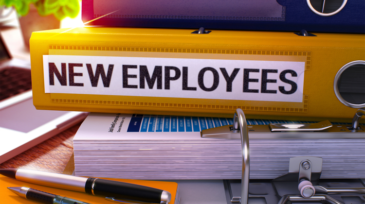 Yellow binder that says "new employees" sits on a desk on top of other binders and papers.