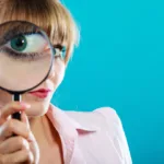 Woman in pink top against blue background holds a magnifying glass up to her eye. It's important to look closely at copywriting courses before buying to make sure you get the steps and support you need.