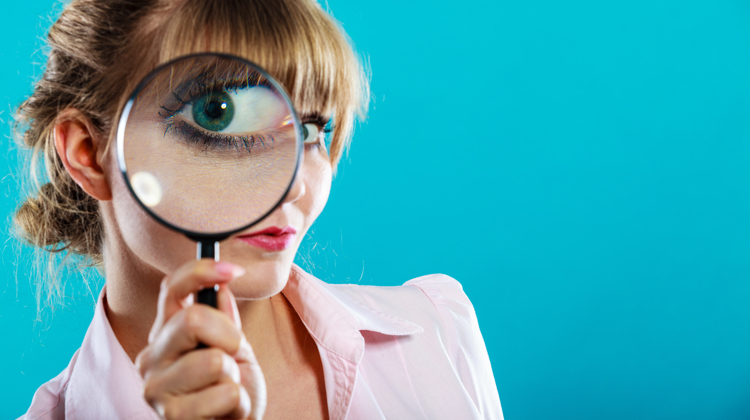 Woman in pink top against blue background holds a magnifying glass up to her eye. It's important to look closely at copywriting courses before buying to make sure you get the steps and support you need.