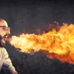 Bearded man wearing a dress shirt and tie breathes fire out of his mouth