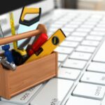 Tiny wooden toolbox filled with mini hammer, saw, level, and other tools sits on top of a laptop keyboard.