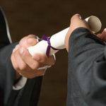 A hand coming out of a black robe hands a rolled up piece of paper tied with a ribbon to another hand in a robe.