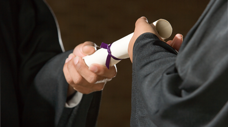 A hand coming out of a black robe hands a rolled up piece of paper tied with a ribbon to another hand in a robe.