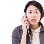 Woman holds up phone on cord to her ear with a look of dismay on face; don't make this sales call mistake if you want to land copywriting clients