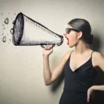 Woman in sunglasses with black dress yelling into megaphone