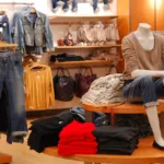 image of a clothing store with racks of clothes and a mannequin sitting on a small table