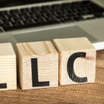 Block letters with "LLC" stand in front of a laptop