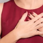 Person with maroon tank top and matching nails holds her hands crossed over her heart.