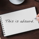 "This is absurd" is written on a notebook that is on a desk.