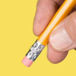 A hand holds a pencil with the eraser side down against a school-bus yellow background.