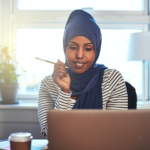 Woman in hijab sits in front of her laptop with pencil in hand
