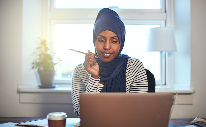 Woman in hijab sits in front of her laptop with pencil in hand