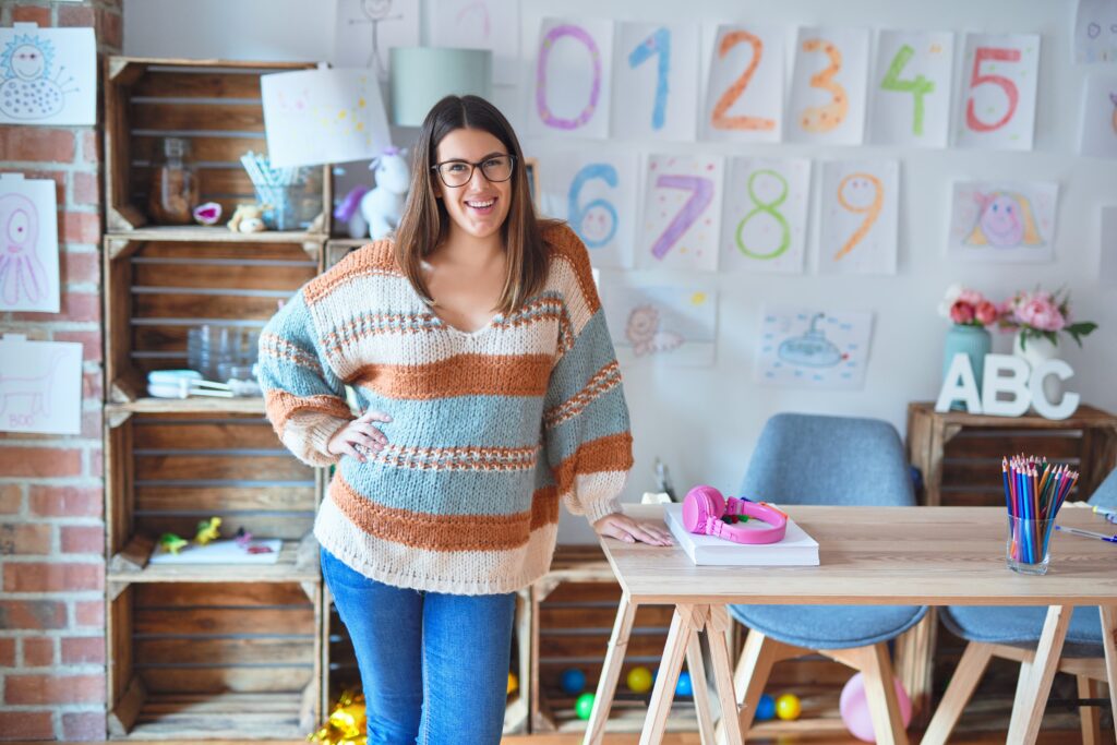 Young woman teacher stands in front of classroom where numbers are on the whiteboard.