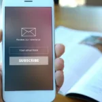 Hand holding white smartphone which has a message on screen "subscribe to our newsletter" with envelope icon and "subscribe" butotn.