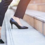 Woman's legs in black dress pants and black high heels walks up concrete steps.