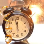 Old fashioned alarm clock is close to midnight with a sparkler behind it and a streamer in front of it.