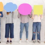 Five people in a row, the first four in jeans and the last in khakis, hold up different shaped and colored thought bubbles to cover their faces.