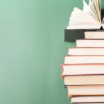 Stack of books against a green background with the top book's pages fanned open.