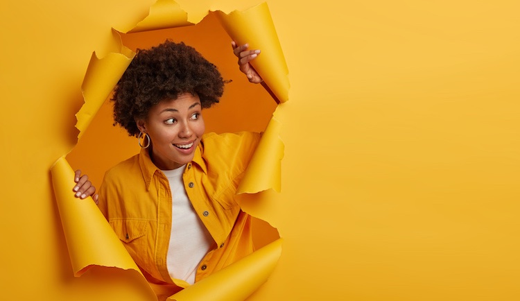 Woman peeks through a hole that looks like ripped paper in a bright yellow. You can break into copywriting, especially if you follow the steps that other successful six-figure copywriters have taken. No need to reinvent the wheel!