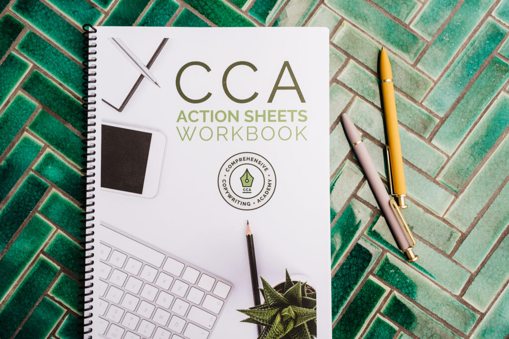 The "CCA Action Sheets Workbook," a valuable part of the copywriting course, sits on a teal tiled table with two beds beside it.