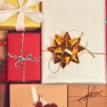 Gifts sitting side-by-side in a variety of wrapping paper—plaid, red, white, gold—and ribbons and bow are shot from above.