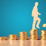 Wooden cutout of a human walks up a pile of gold coins ascending in high from left to right while a hand adds more coins to the last pile.