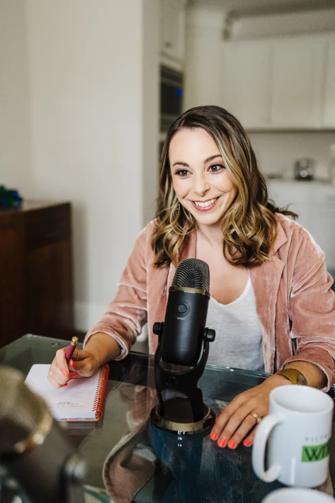 Kate Sitarz, one of the hosts of the Build Your Copywriting Business podcast, sits at a desk with a pen in hand and microphone in front of her.