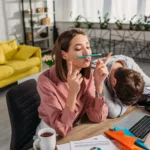 Woman procrastinates by trying to balance a pencil between her nose and lips while a man sits with his head in his arm next to her.