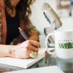 Filthy Rich Writer mug sits on desk while Nicki's hand writes in notebook.