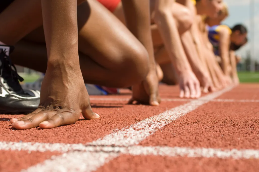 Hands and knees of athletes lined up at the starting line on a track.