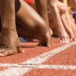 Hands and knees of athletes lined up at the starting line on a track.