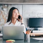 Woman on phone in front of laptop in a home office