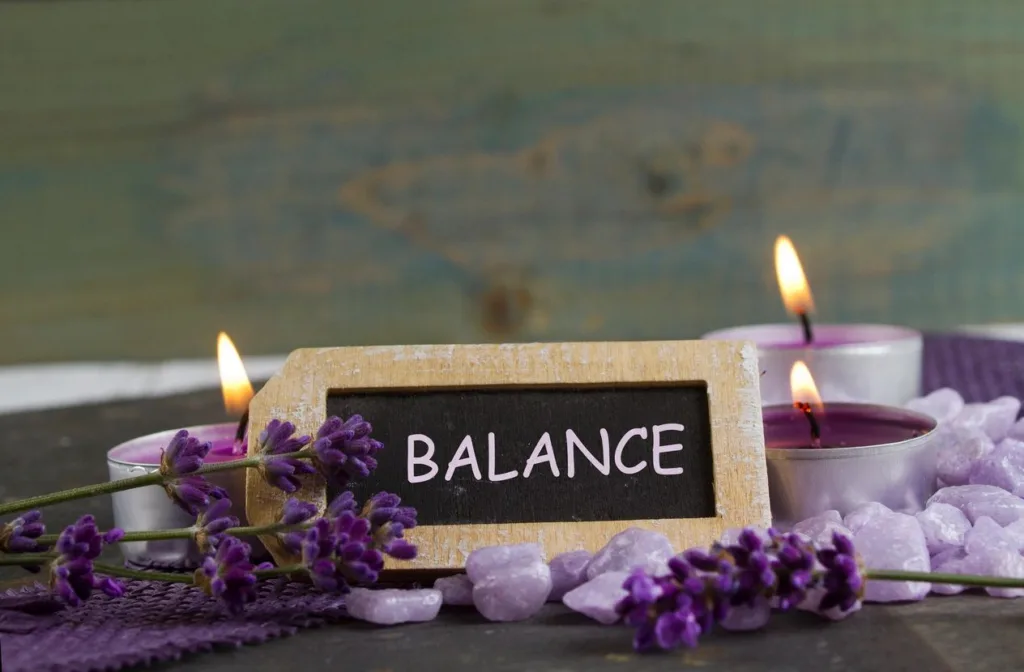 Sign with the word "balance" on in with purple flowers and lit purple candles surrounding it