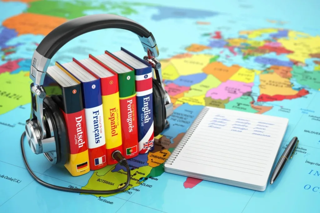 Set of dictionaries in different languages with headphones surrounding them sitting on a map of the world next to a notebook of words