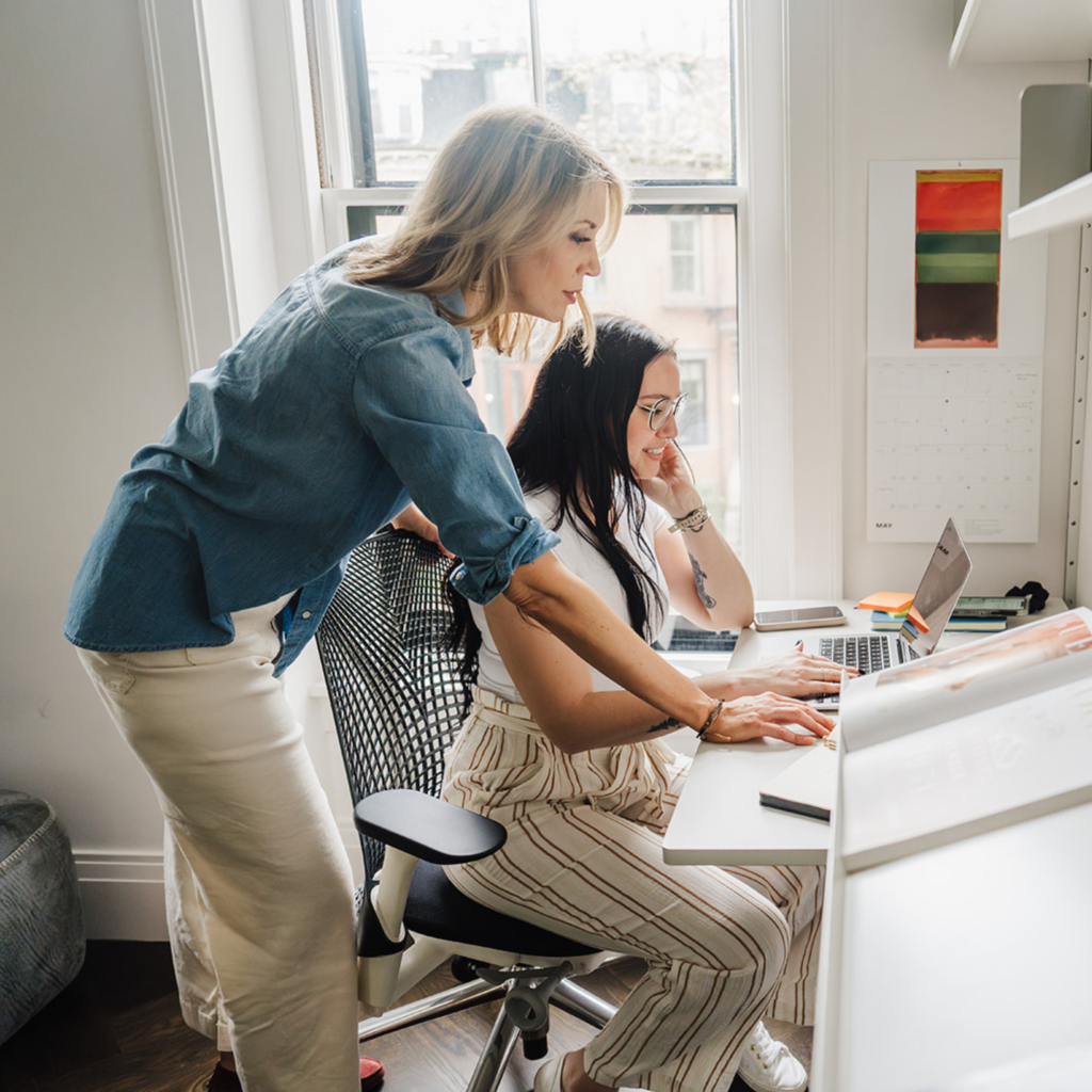 Nicki Krawczyk, founder of Filthy Rich Writer and the Comprehensive Copywriting Academy stands behind a student helping her on the laptop.