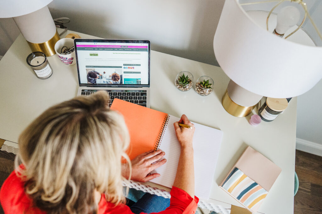 Nicki Krawczyk, founder of the Comprehensive Copywriting Academy, writes in a notebook with her laptop open.