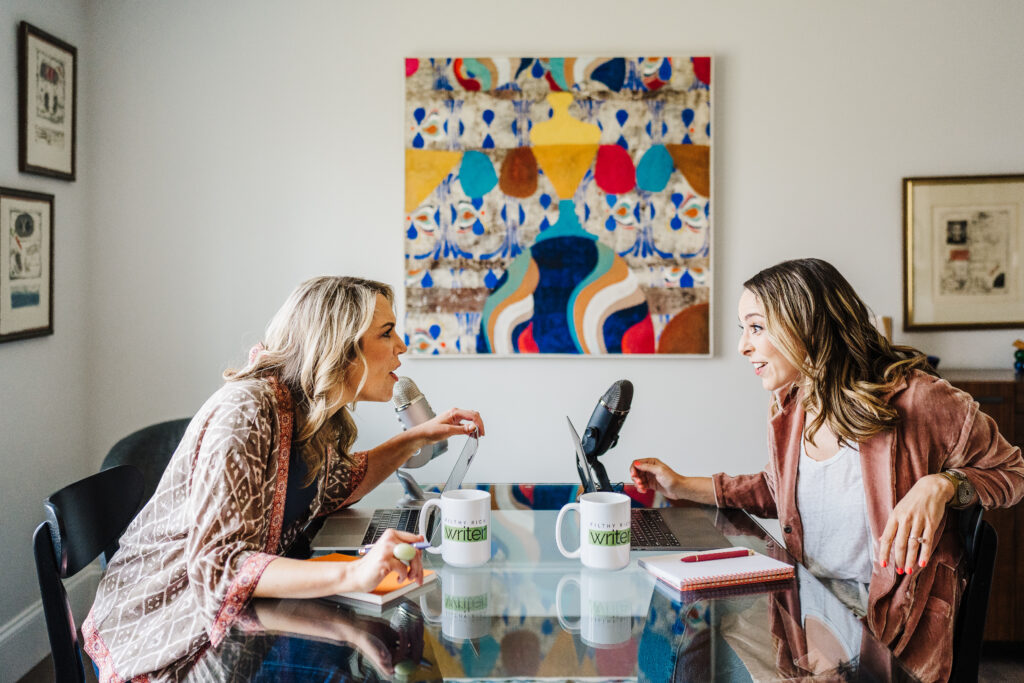 Nicki Krawczyk, founder of the Comprehensive Copywriting Academy, and Kate Sitarz, talk across from each other at a table with a colorful painting in the background.